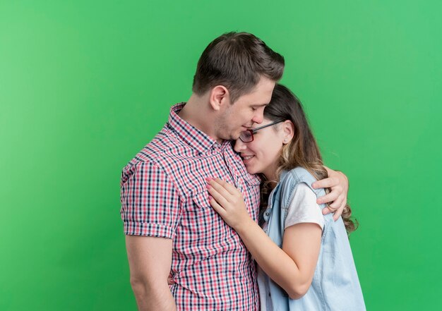 Молодая пара мужчина и женщина в повседневной одежде, счастливые в любви, обнимаются, стоя над зеленой стеной
