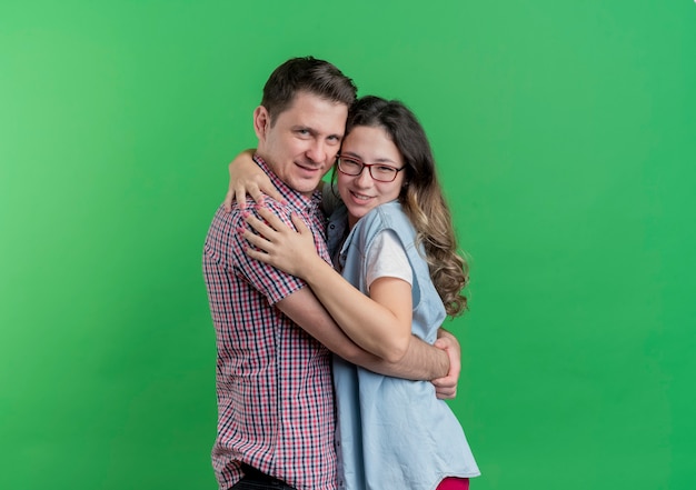 Free photo young couple man and woman in casual clothes happy in love hugging standing over green wall