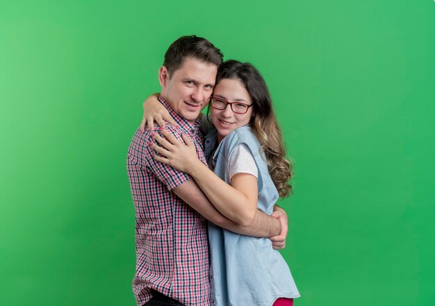 Young couple man and woman in casual clothes happy in love hugging standing over green wall