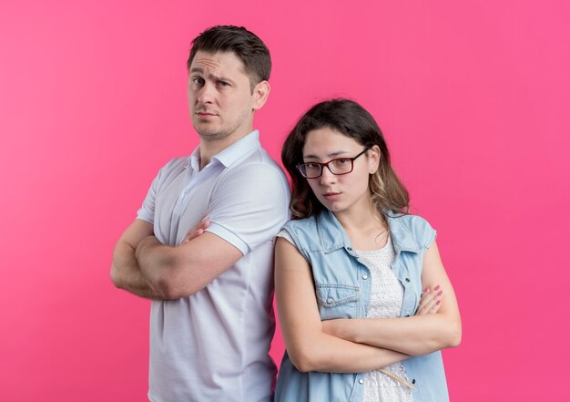 Молодая пара мужчина и женщина в повседневной одежде стоят спиной к спине недовольно и хмуро смотрят на розовую стену