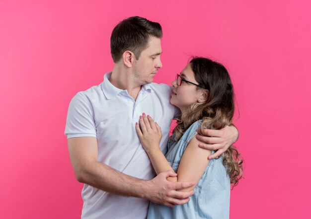 젊은 부부 남자와 여자 캐주얼 옷을 함께 서 행복 나는 분홍색 벽 위에 포옹 사랑