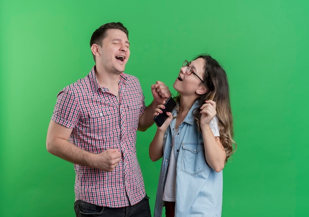 Giovane coppia uomo e donna in abiti casual che stanno insieme divertendosi felice e gioioso sopra la parete verde