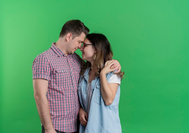 Young couple man and woman in casual clothes standing together hugging happy in love over green wall