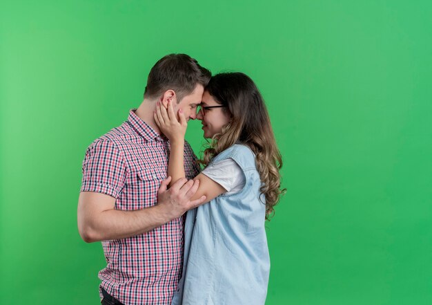緑の壁に恋をして幸せに抱き合って一緒に立っているカジュアルな服を着た若いカップルの男性と女性