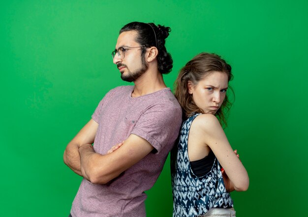 young couple man and woman frowning while standing back to back during fight over green wall