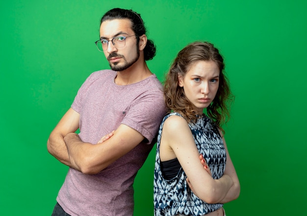 young couple man and woman frowning while standing back to back over green wall