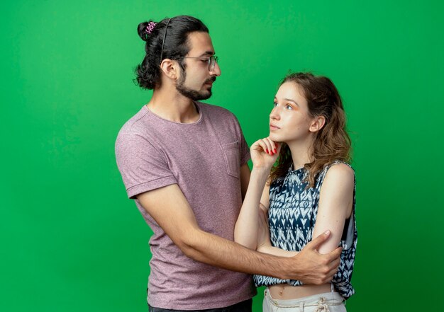 young couple man and woman happy man hugging his girlfriend while she standing with pensive expression over green wall