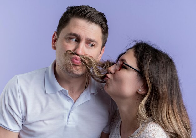 Young couple man and woman having fun together standing over blue wall