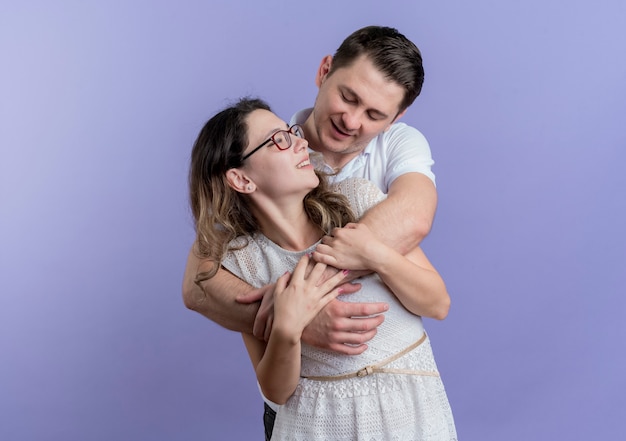 Young couple man and woman hugging happy in love smiling cheerfully over blue