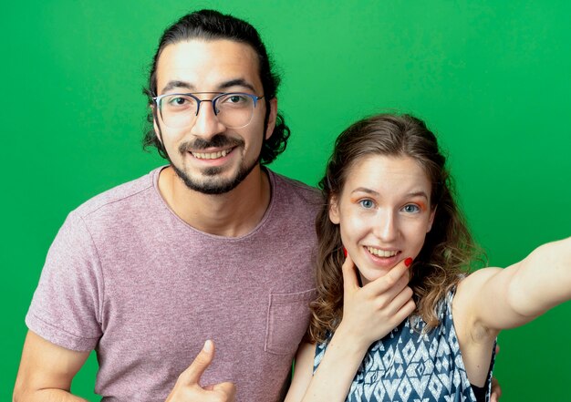 Young couple man and woman, lookign at camera smiling with happy faces standing over green background