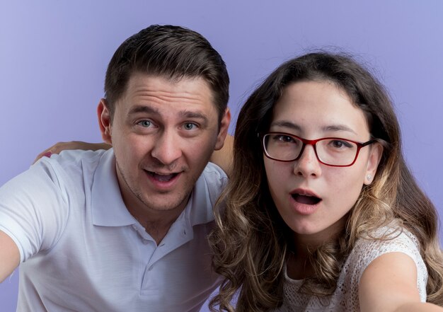 Young couple man and woman looking at camera smiling happy and positive over blue wall