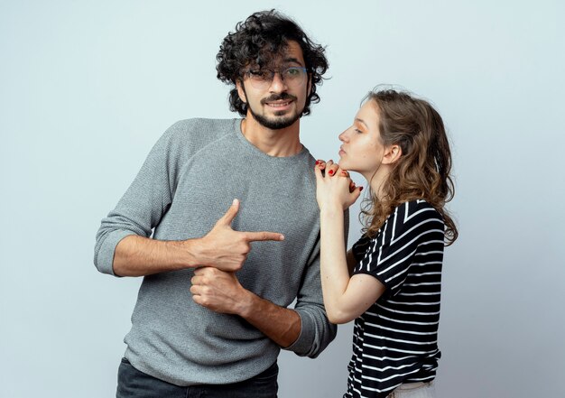 Young couple man and woman, woman touching shoulder of her boyfriend while he pointing with finger to her standing over white background