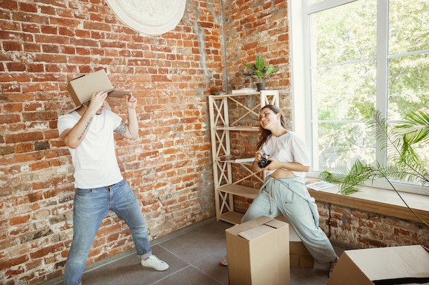 Young couple moved to a new house or apartment. Having fun with cardboard boxes, relaxing after cleaning and unpacking at moved day. Look happy. Family, moving, relations, first home concept.