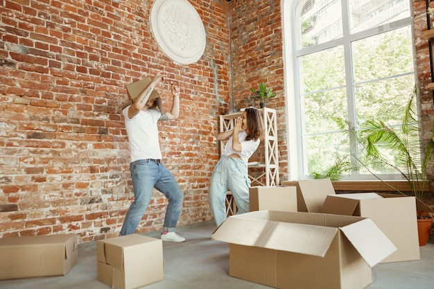 Young couple moved to a new house or apartment. Having fun with cardboard boxes, relaxing after cleaning and unpacking at moved day. Look happy. Family, moving, relations, first home concept.