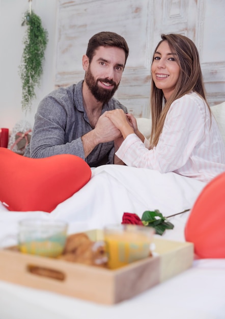 Young couple in pajamas holding hands on bed 