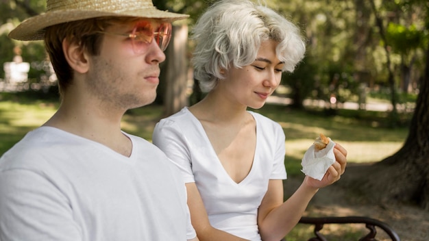 Giovani coppie al parco che mangiano hamburger insieme