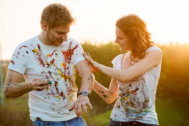 Young couple playing with paint at sunset