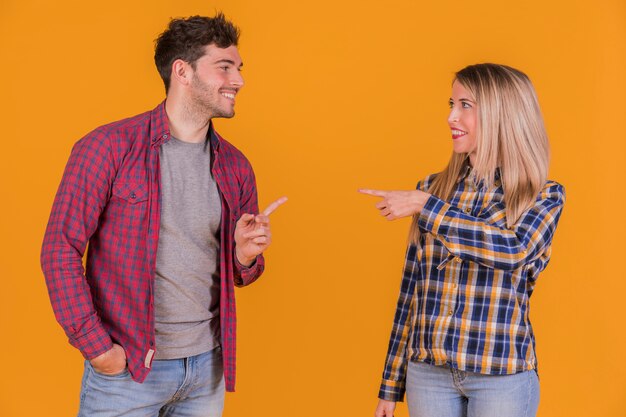 Young couple pointing their fingers to each other against an orange backdrop