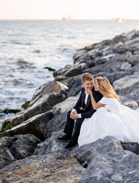 岩の上に座っている海に対してポーズをとる若いカップル