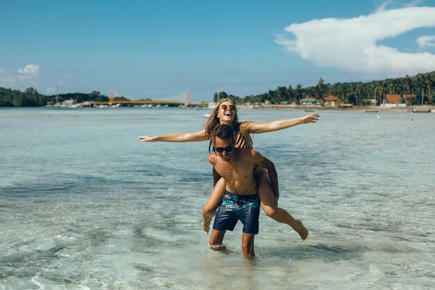 молодая пара, создает на пляже, с удовольствием в море, смеясь и улыбается