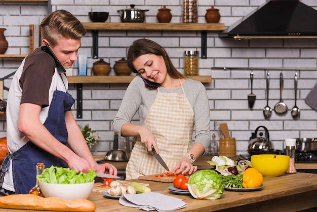 Young couple preparing salad during smartphone conversation