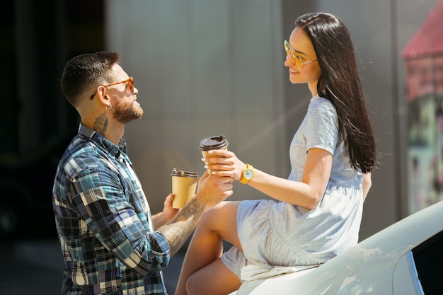 Foto gratuita giovani coppie che preparano per il viaggio di vacanza in macchina in una giornata di sole. donna e uomo che bevono caffè e pronti per andare al mare o all'oceano.