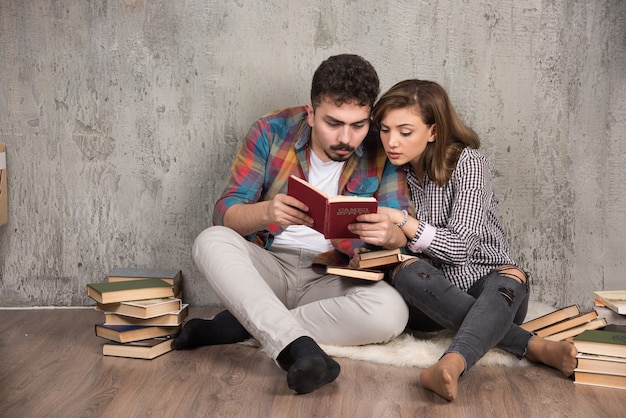 Young couple reading an interesting book while sitting on floor