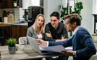 Free photo young couple and real estate agent using laptop while going through housing plan on a meeting