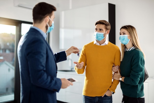 Young couple receiving key of their new home from real estate agent during COVID19 pandemic