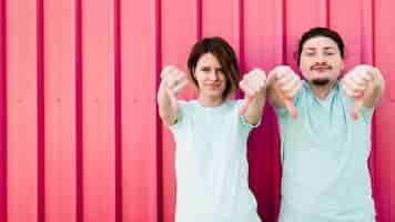 Free photo young couple showing their thumb downs against corrugated iron metal sheet