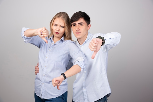 Молодая пара показывает палец вниз с отрицательным выражением лица.