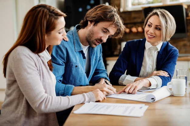 Young couple signing lease agreement while having meeting with real estate agent Focus is on man