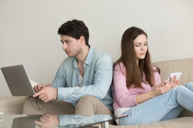Young couple sitting back to back using laptop computer