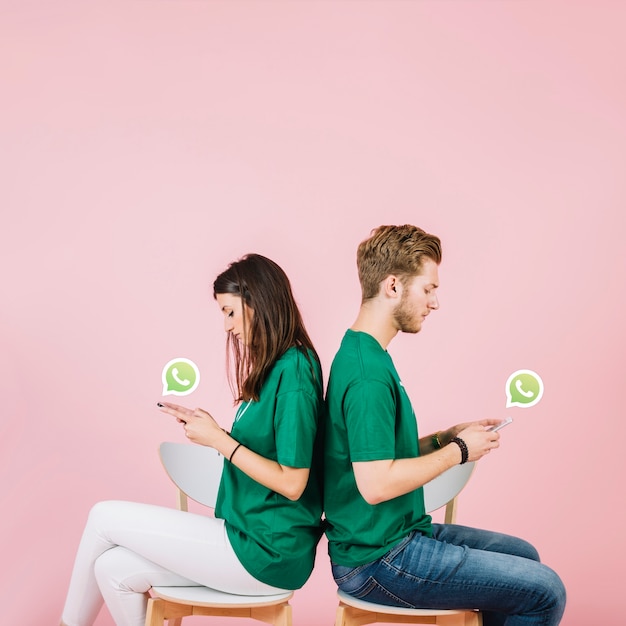 Young couple sitting back to back using whatsapp on smartphone