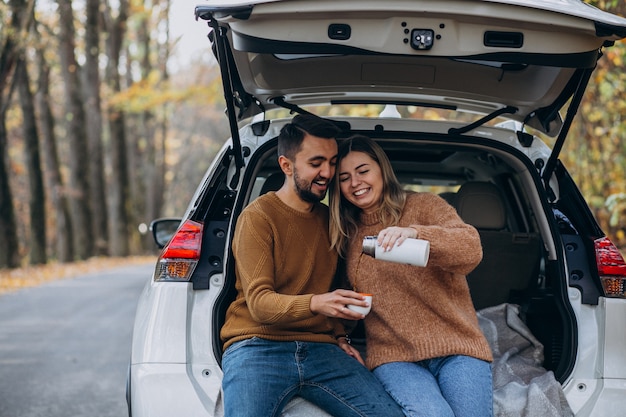 Young couple sitting at the back of a car drinking tea in forest