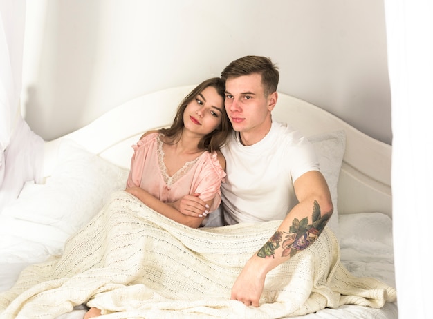 Молодая пара сидит на кровати под одеялом