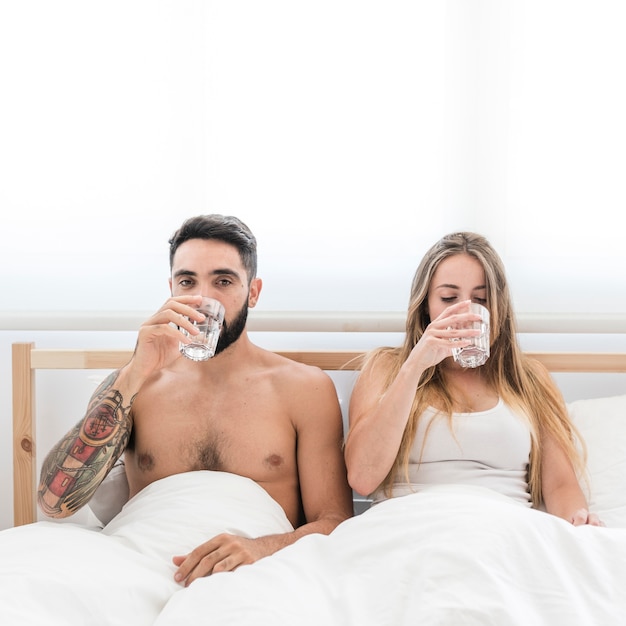 Young couple sitting on bed drinking glass of water