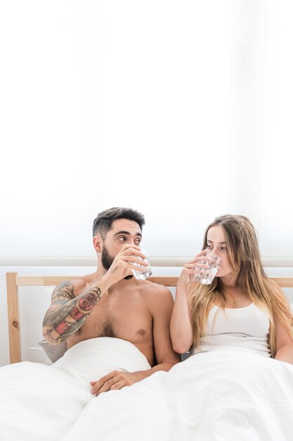 Young couple sitting on bed drinking water