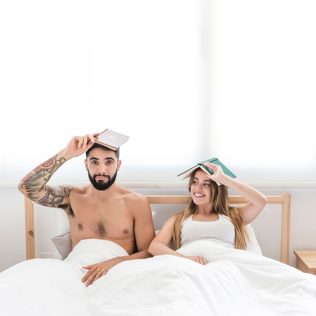 Young couple sitting on bed holding book over their head