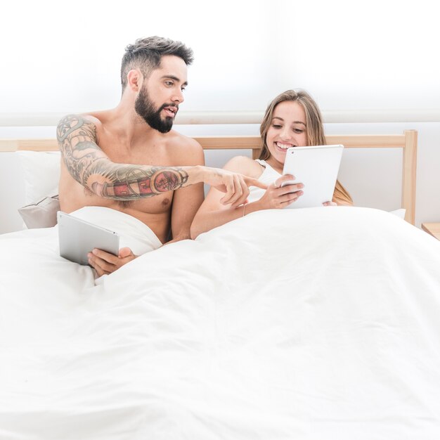 Young couple sitting on bed using cellphone
