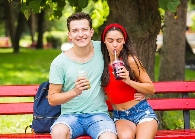 公園で健康なスムージーを飲むベンチに座っている若いカップル