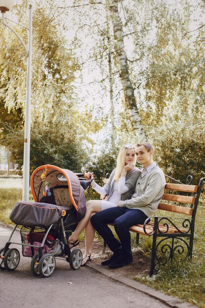 Молодая пара сидит на скамейке в парке с ребенком корзину рядом
