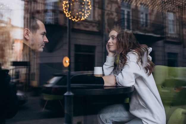 Free photo young couple sitting in a cafe behind the window