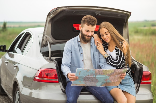 Young couple sitting in the car trunk looking at map