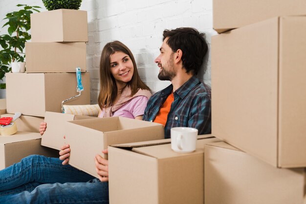 Young couple sitting between the cardboard boxes looking at each other