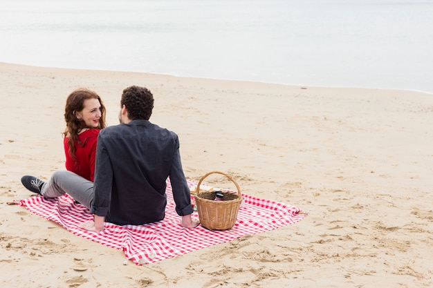 Young couple sitting on coverlet on sea shore 