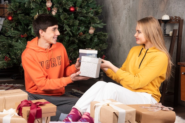 젊은 부부는 바닥에 앉아서 크리스마스 인테리어에서 서로에게 선물을 주고 있다