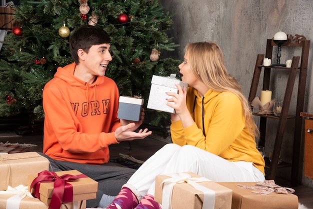 Young couple sitting on the floor and holding presents in Christmas interior