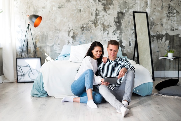 Young couple sitting on floor and using tablet