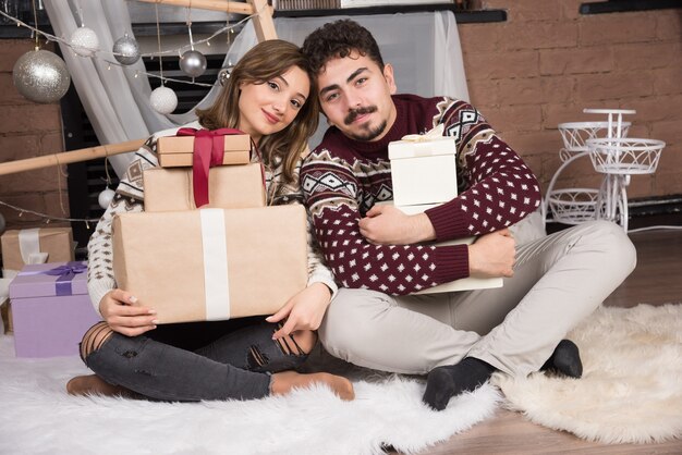 Молодая пара, сидя на полу с подарками коробки в интерьере Рождества.